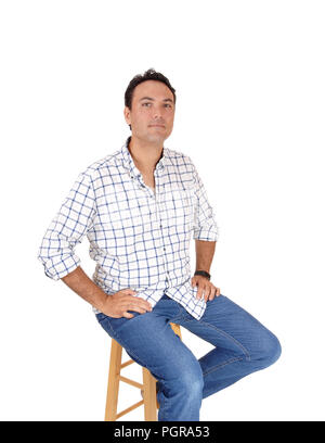 Un portrait d'une jeune mans assis dans une chemise à carreaux et jeans sur une chaise, à la recherche dans l'appareil photo, isolée pour fond blanc Banque D'Images