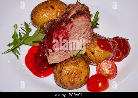 Grande paix de la viande de mouton bien moyen rôti avec des pommes de terre, tomate fraîche et sauce airelle rouge sur la plaque blanche Banque D'Images