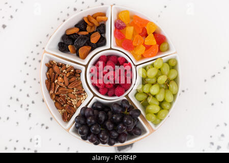 Ensemble de plaques rondes plein de noix, bonbons, framboises, raisins et fruits secs sur le fond blanc. Des collations santé. Desserts pour un café ou un thé. Asso Banque D'Images