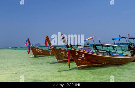 Trois longs bateaux off attachés près de la plage avec vue sur l'océan et les rochers au loin. Banque D'Images