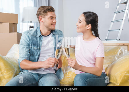 Beau jeune couple clinking glasses of champagne, assis sur table à un nouveau foyer Banque D'Images