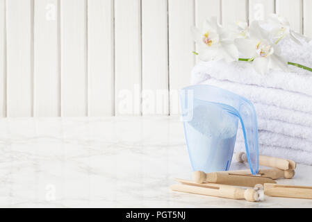 Tasse à mesurer en plastique bleu avec du détergent, pile de serviettes blanches et pinces à linge en bois, fleur d'orchidée blanche sont sur une surface en marbre contre Banque D'Images