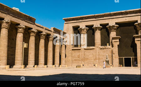 Garde égyptienne en uniforme blanc marchant dans la cour des offrandes avec des colonnes palmiformes, Temple d'Edfu, Egypte, Afrique Banque D'Images