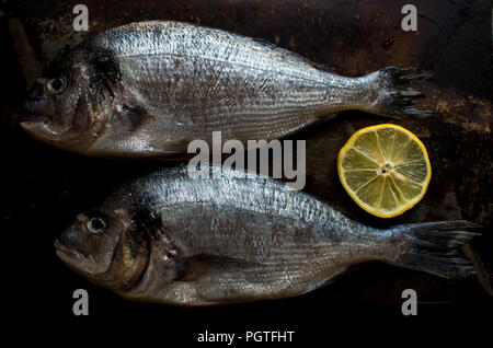 Deux poissons crus avec du citron sur le fond noir Banque D'Images