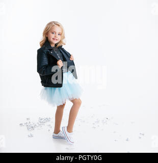 Belle petite fille aux cheveux bouclés blonde hairstyle emplacement sur la fête de Noël en robe avec paillettes et veste noire. Feuille d'argent sur le sol. Concep Banque D'Images