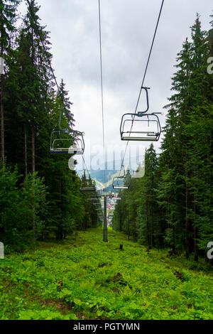 Télésièges dans le Ski d'été pluvieux à travers les montagnes de la forêt de montagne fabuleux incroyable en Bukovel, Carpates ukrainiennes Banque D'Images