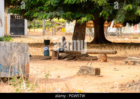 BUBAQUE, GUINÉE BISSAU - 5 mai 2017 : local non identifié petit garçon est assis sur le banc en bois dans un village de l'île de Bubaque. Les gens de G.-Bissau s Banque D'Images