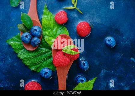 Les baies d'été dans des cuillères en bois Vue de dessus. Mélange de bleuets et framboises sur un fond bleu foncé avec copie espace humide. Les ingrédients bruts d'en haut Banque D'Images