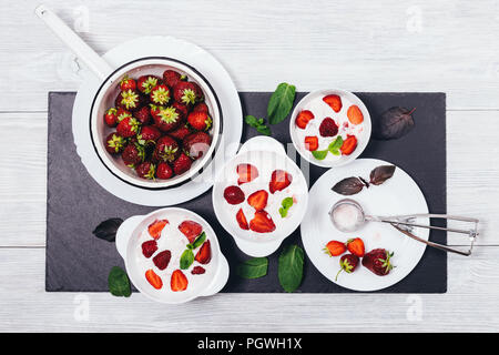 Télévision lumineuse composition laïcs froid préparation desserts aux fruits. Glace maison bols décorés de fraises rouges, feuilles de menthe et de basilic, vue du dessus Banque D'Images