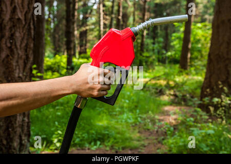 Une main humaine tenant un pistolet de l'essence dans une forêt. Concept, les questions environnementales autour du pétrole. Banque D'Images