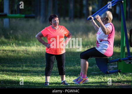 Femme âgée sur l'aire de sport de faire les exercices sur le simulateur avec l'entraîneur. Banque D'Images