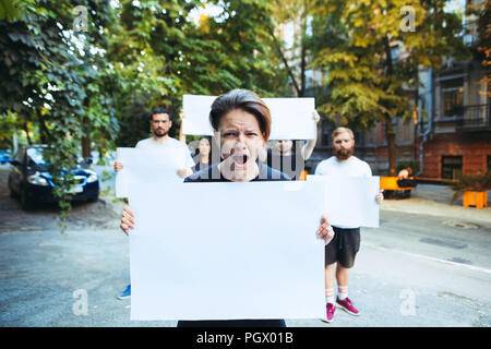 Groupe de jeunes manifestants à l'extérieur. La protestation, les gens, de démonstration, de la démocratie, de la lutte, l'homme, protestant contre le concept. Les hommes de race blanche et womem holding empty des affiches ou des bannières avec copie espace Banque D'Images