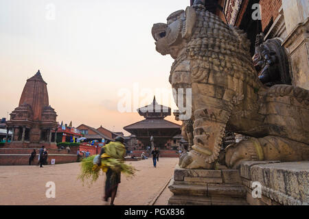 Bhaktapur, Vallée de Katmandou, Népal Bagmati, : Un homme passe devant les statues de lion en dehors du palais royal au coucher du soleil à Durbar Square au monde de l'Unesco Banque D'Images