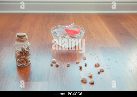 Still Life composition du bol en verre avec de l'eau et de deux navires, les coquillages papier conçu autour sur le sol. Voyage de rêve et d'aventure concept Banque D'Images