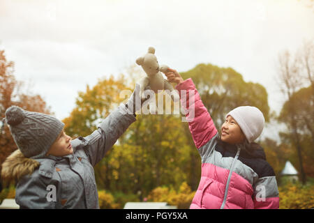 Jeune garçon et fille augmentant leur part en maintenant teddybear durant le frisson dans park Banque D'Images