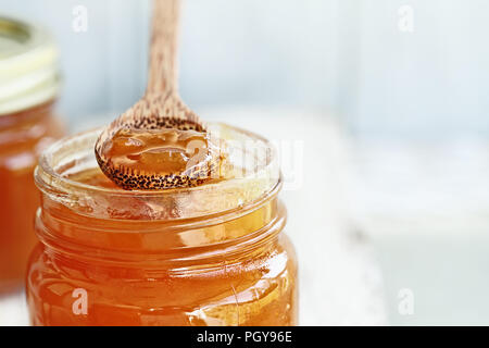 Vue de face de la pointe d'une cuillère en bois plein de confiture de cantaloup maison reposant sur un pot ouvert rempli de confiture. Banque D'Images