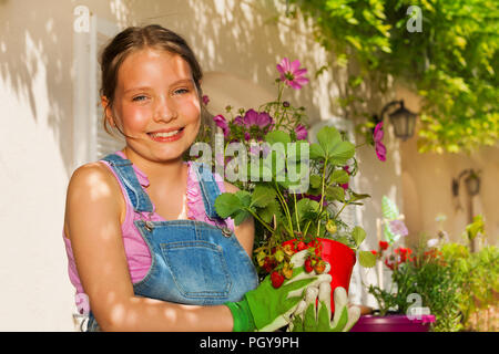 Close-up portrait of beautiful preteen girl, debout sur le balcon Jardin et holding potted plants de fraises Banque D'Images