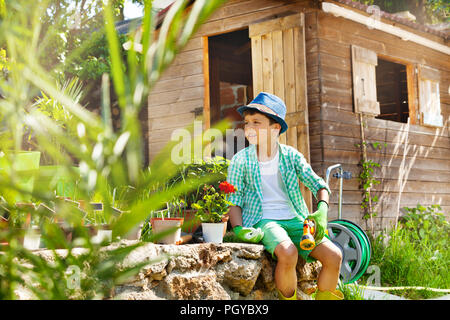 Portrait de jeune garçon de sept ans, portant chapeau et des gants, travaillant en journée ensoleillée au jardin Banque D'Images