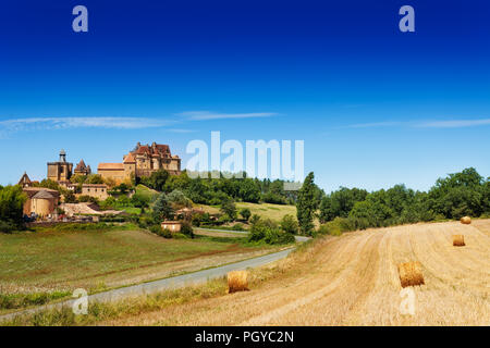 Paysage d'été campagne avec des balles de foin sur le domaine et château de Biron sur la colline en arrière-plan, France, Europe Banque D'Images