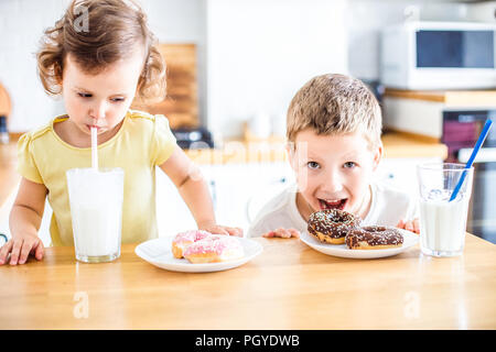 Les enfants de manger des beignes et boire du lait sur la cuisine à la maison blanche. Enfant s'amuse avec les beignets. La nourriture bonne pour les enfants. Banque D'Images