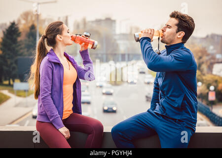 La femme et l'homme de l'eau potable dans les pause dans la formation de forme physique avec un paysage urbain dans l'arrière-plan Banque D'Images