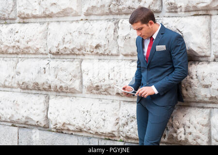 Young handsome businessman en costume et cravate de la lecture d'un comprimé contre le mur de marbre Banque D'Images