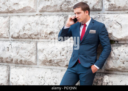 Young handsome businessman en costume et cravate à parler le smartphone contre un mur en marbre Banque D'Images