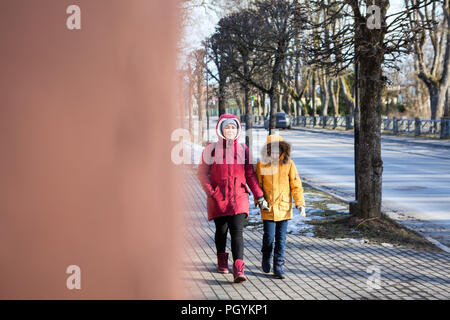 Mère en veste rouge et sa jeune fille en jaune la marche sur la rue en milieu urbain, vue à partir de l'angle Banque D'Images