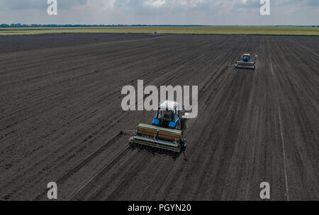 Deux tracteur bleu vif de labourer le sol contre un arrière-plan de la terre noire. Banque D'Images