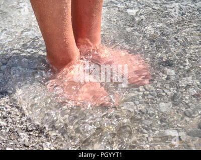 Hairy strong male legs are cooling in cold water of mountain lake. Green blue cold water of kaje in Dolomiti. Banque D'Images