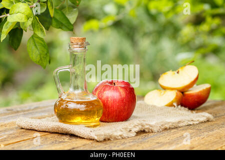 Vinaigre de pomme dans le flacon en verre avec bouchon et fresh red apple sur le sac et la vieille planches en bois avec fond naturel brouillée. Les aliments biologiques Banque D'Images