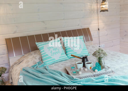 Une chambre confortable avec des tasses à café, des fleurs sauvages sur une planche en bois au lit à la maison. Petit-déjeuner romantique, le repos, la relaxation, l'amour. Maison en bois Banque D'Images