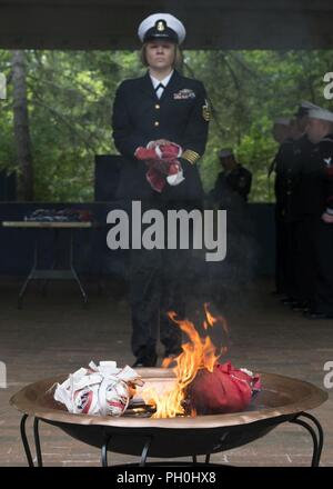 BANGOR, Washington (14 juin 2018) Chef de l'Hospital Corpsman Farrah Ocasio, de Detroit, Michigan, attribué à Trident Centre de formation à Bangor, Washington, les promenades les restes d'un drapeau des États-Unis d'un incendie au cours d'une cérémonie à la retraite drapeau Naval Base Kitsap - Bangor. Lorsqu'un drapeau des États-Unis est usé, déchiré, délavées ou très sale, le drapeau doit être à la retraite dans la dignité et le respect qui sied à elle. La méthode traditionnelle est de couper le drapeau en morceaux, séparant les bandes 13 à partir de canton et leur incinération séparément de façon respectueuse. Banque D'Images