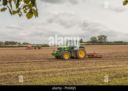 L'agriculture britannique, deux tracteurs John Deere au travail le sous-solage et semis monograine un champ moissonné Banque D'Images