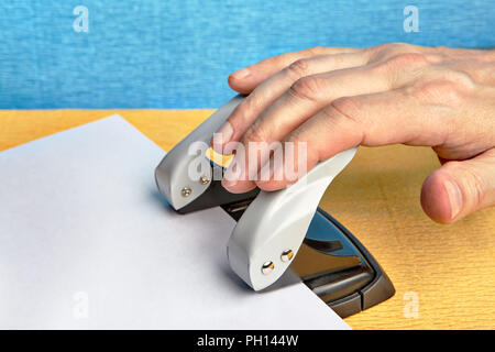 Une main d'homme appuie sur un trou de poinçon qui fait des trous dans un morceau de papier. Banque D'Images