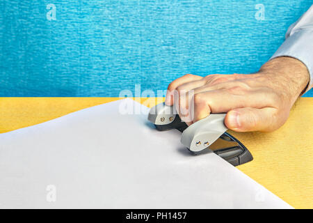 Vivement la main de l'homme appuie sur un poinçon et fait des trous dans un papier. Banque D'Images