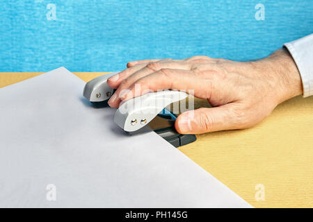 La main de l'homme appuie sur un poinçon et fait des trous dans un papier avec un espace libre. Banque D'Images