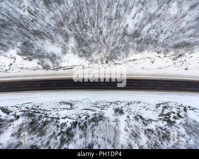 Vue de dessus à la route glissante d'hiver en passant par les forêts de conifères couverts de neige en montagne Banque D'Images