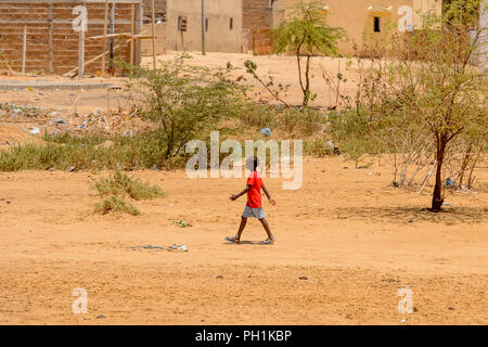 Route de LAMPOUL, SÉNÉGAL - Apr 23, 2017 : petit garçon sénégalais non identifiés en chemise rouge et gris short promenades le long de la rue. Encore beaucoup de gens dans Banque D'Images