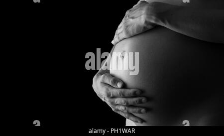 Image en niveaux de gris de la femme enceinte tenant son ventre tendrement attentivement en tournant à son enfant à naître. Banque D'Images