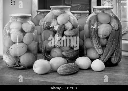 Accueil préservation : grands pots en verre rouge avec des tomates mûres et concombres, scellée. metallid Image noir et blanc. Banque D'Images