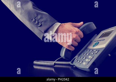 Image Retro de businessman making a phone call tenant le combiné récepteur d'un téléphone à la main , Vue en gros plan de sa main dans un costume. Banque D'Images