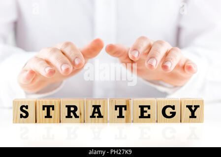 Homme tenant ses mains de manière protectrice sur le mot stratégie sur une rangée de cubes en bois dans une image conceptuelle, libre des cubes et les mains. Banque D'Images