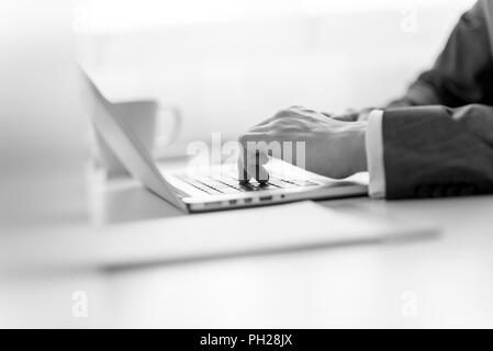 Vue rapprochée de la main d'un businessman en costume à entrer des données sur un ordinateur portable dans un focus sélectif de gris. Banque D'Images