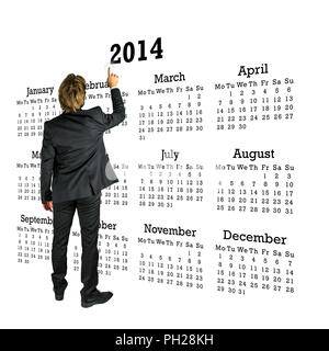 Businessman en costume debout avec son dos à la caméra en face d'un calendrier 2014 sur un fond blanc en pointant sur l'année avec son doigt. Banque D'Images