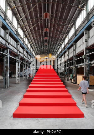 L'Allemagne, Leipzig. Août 24, 2018. Une femme marche le long d'une installation semi-finis par Victor Freso, un immense escalier rouge. Le Festival d'Art Urbain 'Monumenta' ouvre le 1er septembre dans l'usine vide de l'ex-Pittlerwerke salles. La Monumenta présente le graffiti, le street art et l'art contemporain autour de 6 000 mètres carrés jusqu'au 13 octobre. Crédit : Jan Woitas/dpa-Zentralbild/dpa/Alamy Live News Banque D'Images