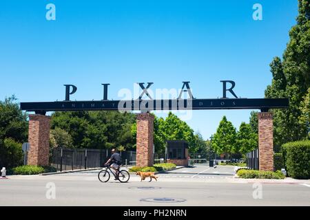 Un homme chevauche son vélo et promène son chien au-delà de l'entrée au siège de Pixar Animation Studios dans le centre-ville d'Emeryville, Californie, avec logo visible, 12 juin 2018. () Banque D'Images