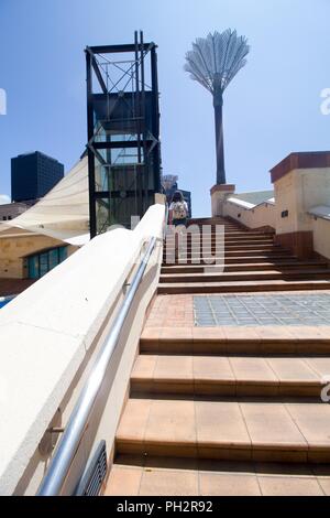 Une femme marche d'un escalier d'élaborer sous un soleil éclatant en Civic Square, Wellington, Nouvelle-Zélande, le 28 novembre 2017. () Banque D'Images