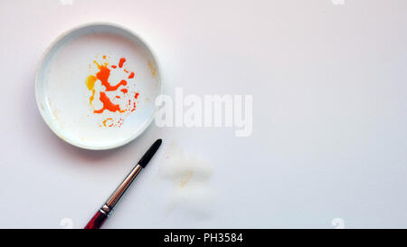 Mise à plat de la couleur de l'eau pinceau et d'un bac de mélange avec de la peinture orange, sur un fond de papier blanc Banque D'Images