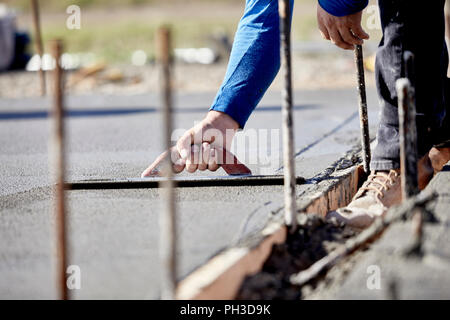 Un maçon à l'aide d'une truelle en béton pour terminer une nouvelle dalle en béton coulé avec une faible profondeur de champ Banque D'Images